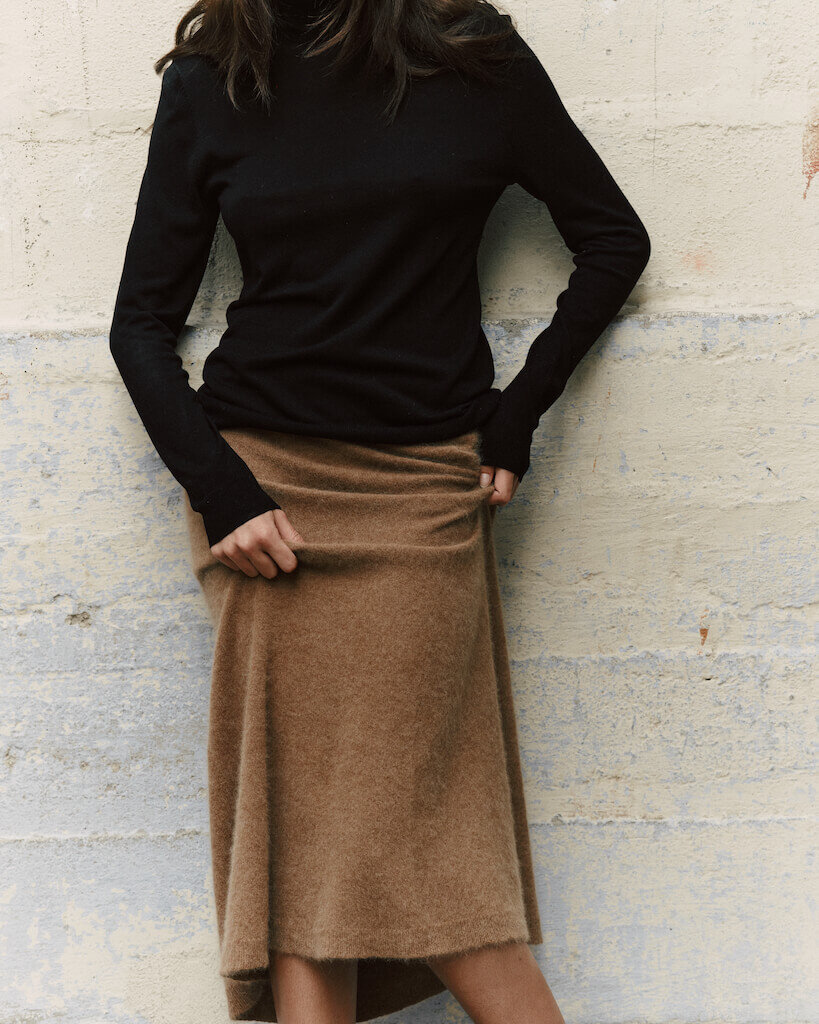 Model in a black silk turtleneck and golden beige knitwear midi skirt by atthrea.
