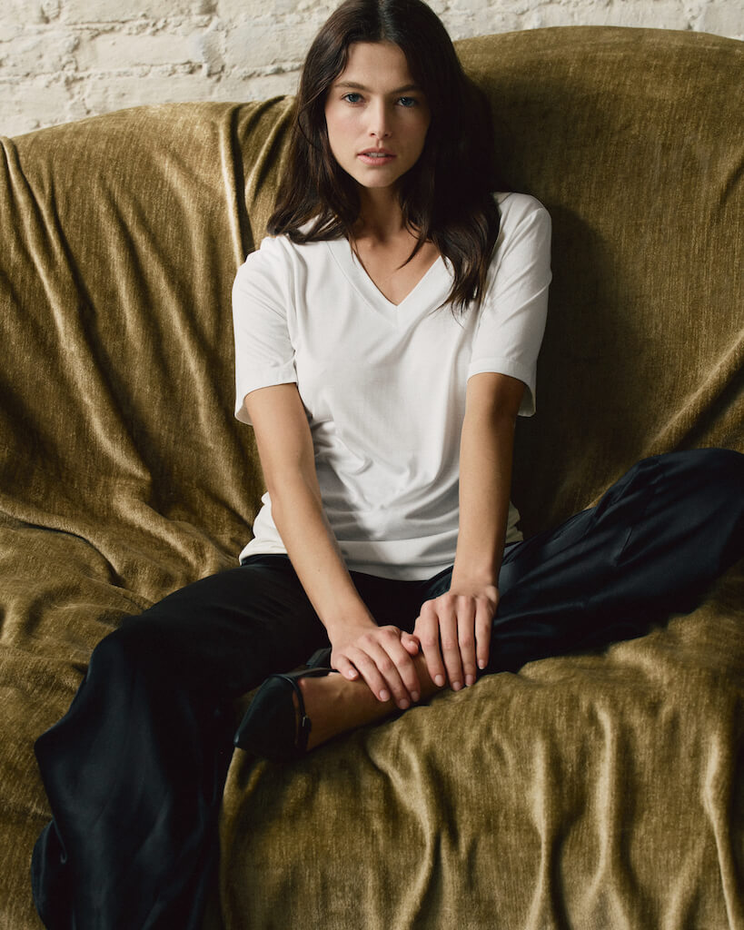 Modell sitzt in entspannter Pose, trägt ein elfenbeinfarbenes Seiden-T-Shirt und schwarze Seidenhosen von Atthrea.