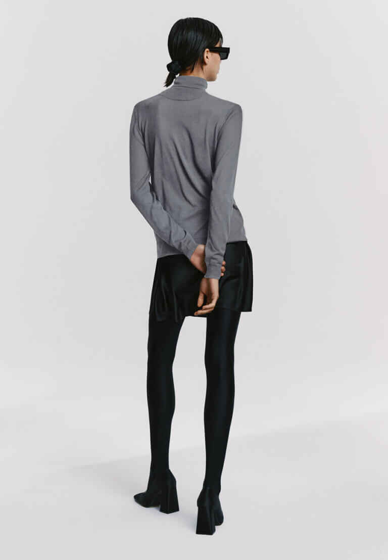 Rear view of Atthrea's grey silk turtleneck styled with silk skirt